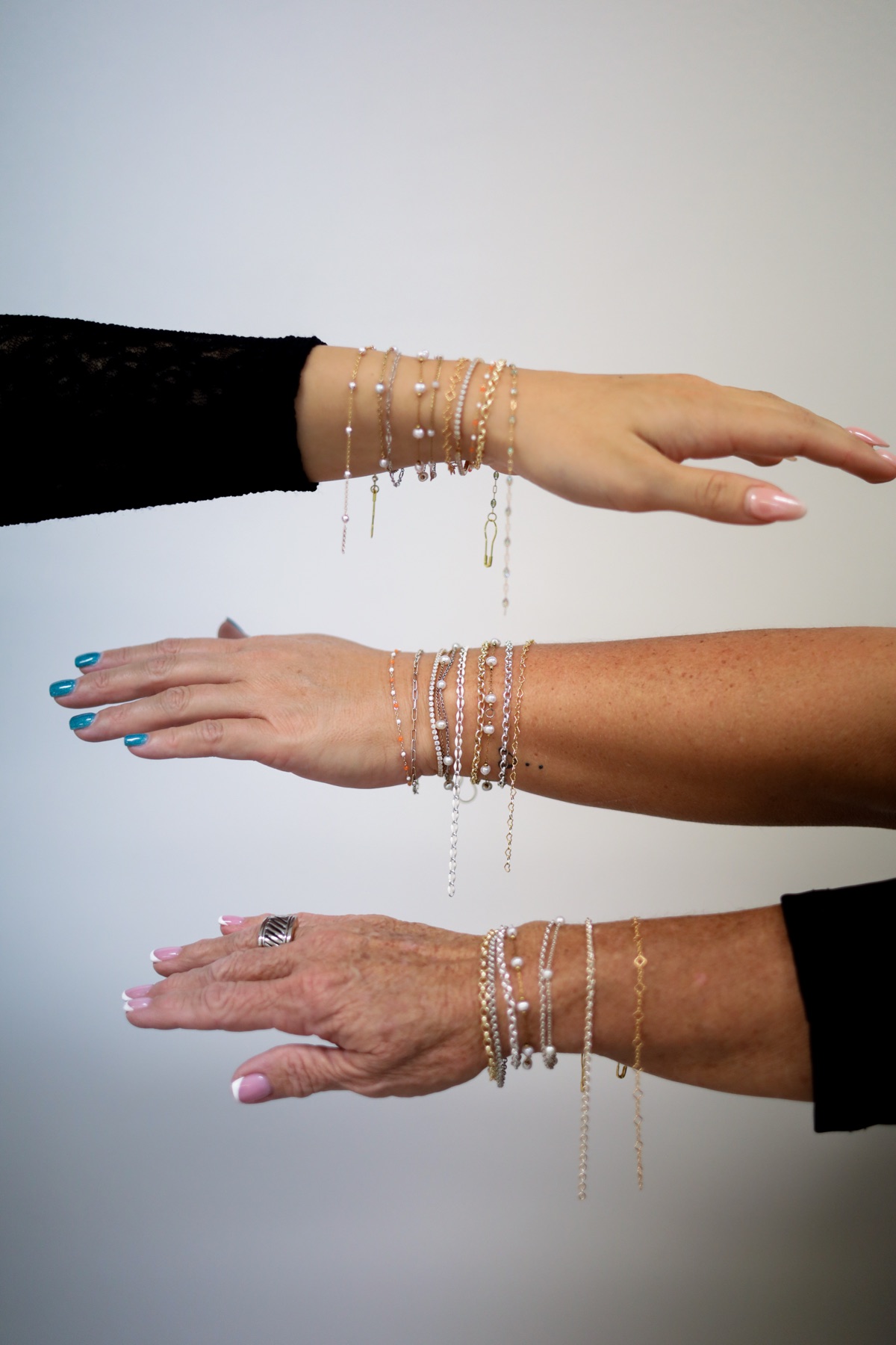 Three arms wearing stacked permanent bracelets